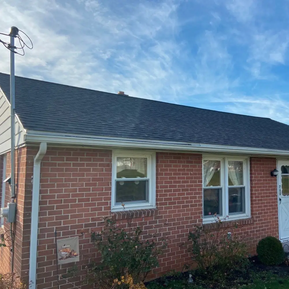 The side of a brick house with a new black roof and white gutters