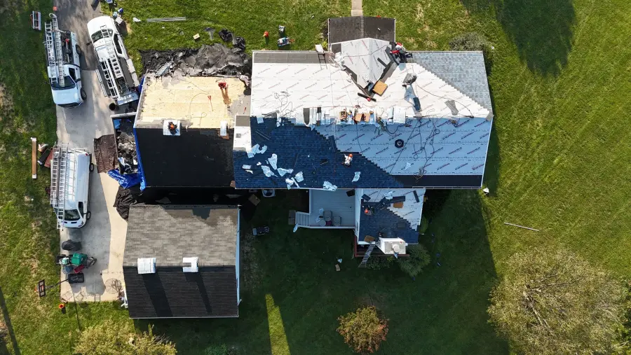 A drone view of a Happy Home crew part way through a roof replacement, with the trailers in the drive