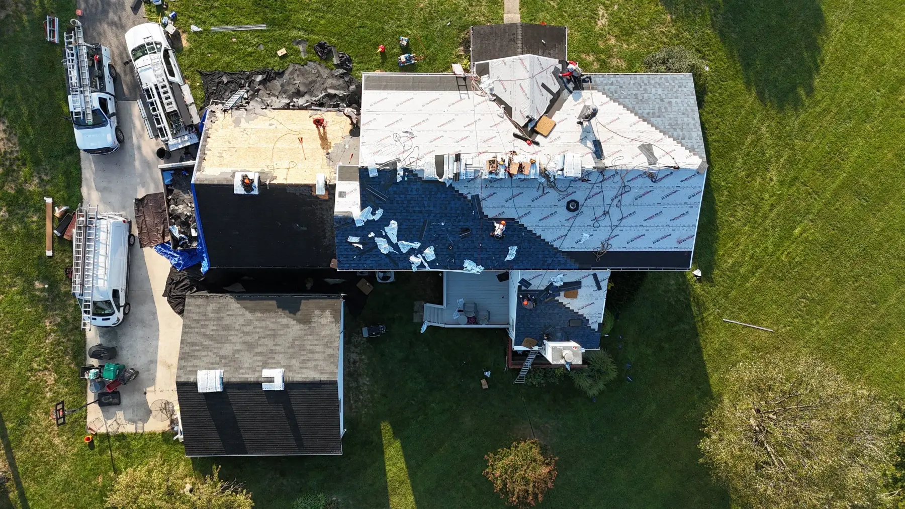 A drone view of a roof replacement in progress, with the trailers in the drive