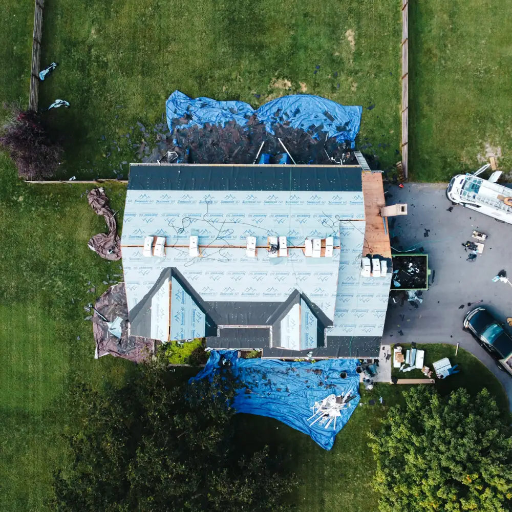 A drone view of a tear-off with blue tarps laid over the yard to catch debris