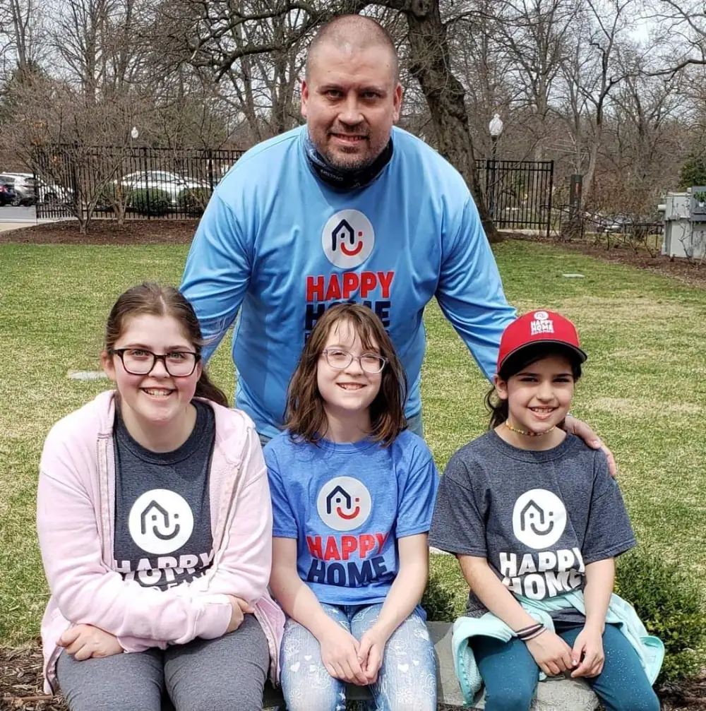 A man and three girls in Happy Home shirts, outdoors on a lawn