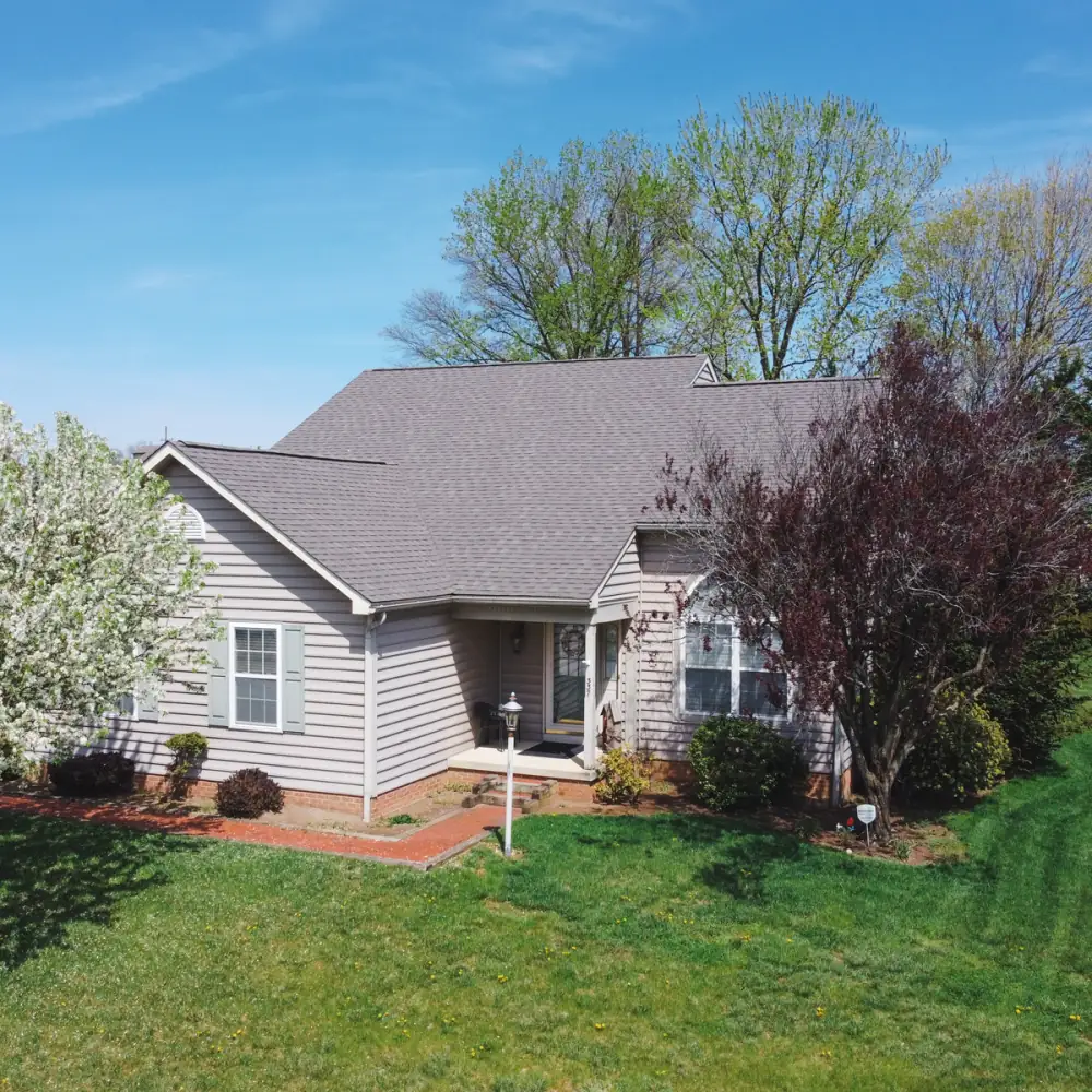 A grey-sided house with a new roof, a blossoming tree beside it
