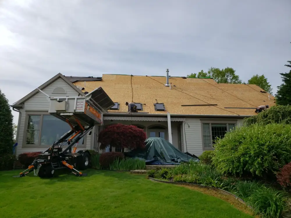 A material lift beside a house with its roof stripped to the deck