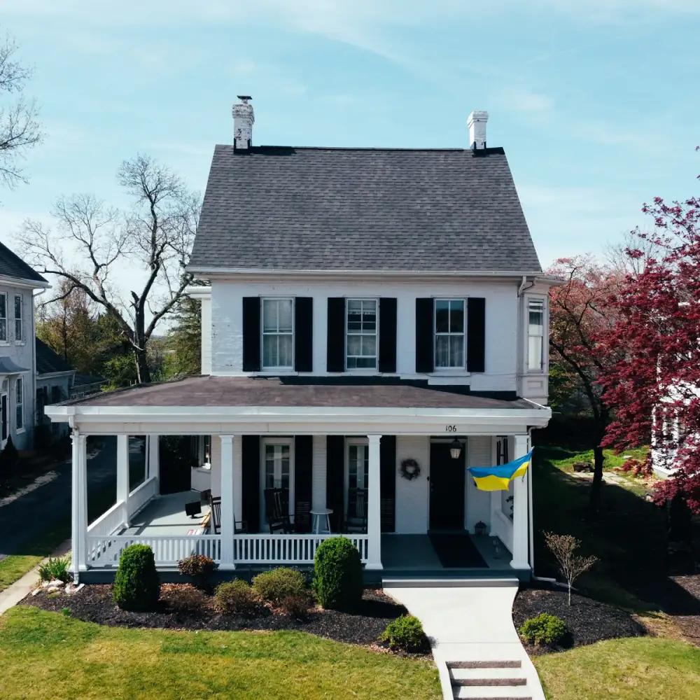 A white two-storey house with black shutters, a porch and a new grey roof
