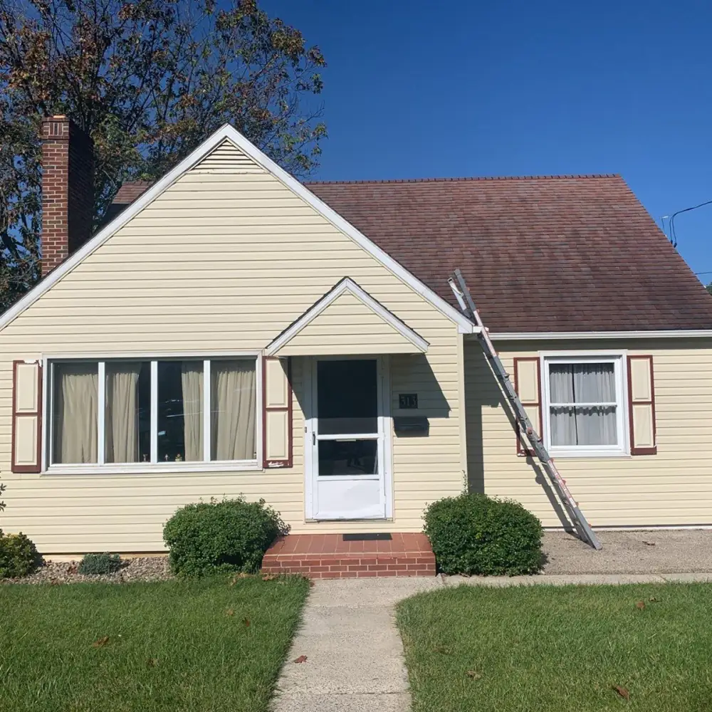 A yellow Cape Cod house with a ladder against the roof, before its new roof